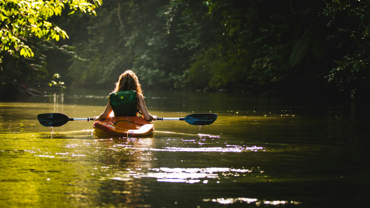 Woman paddling a kayak on calm water holding a double-bladed paddle