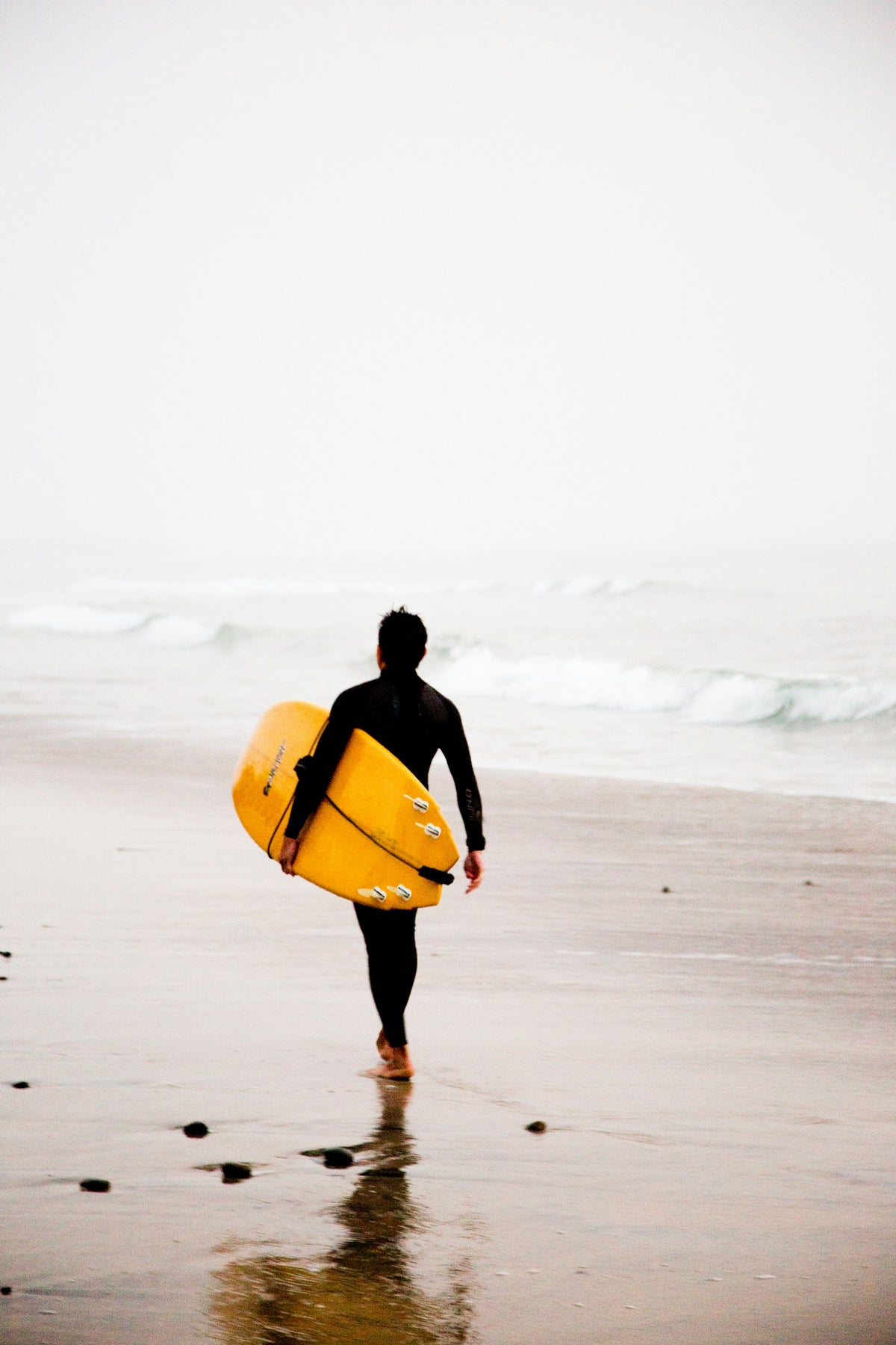 Surfer carrying a yellow surfboard while walking along the shoreline