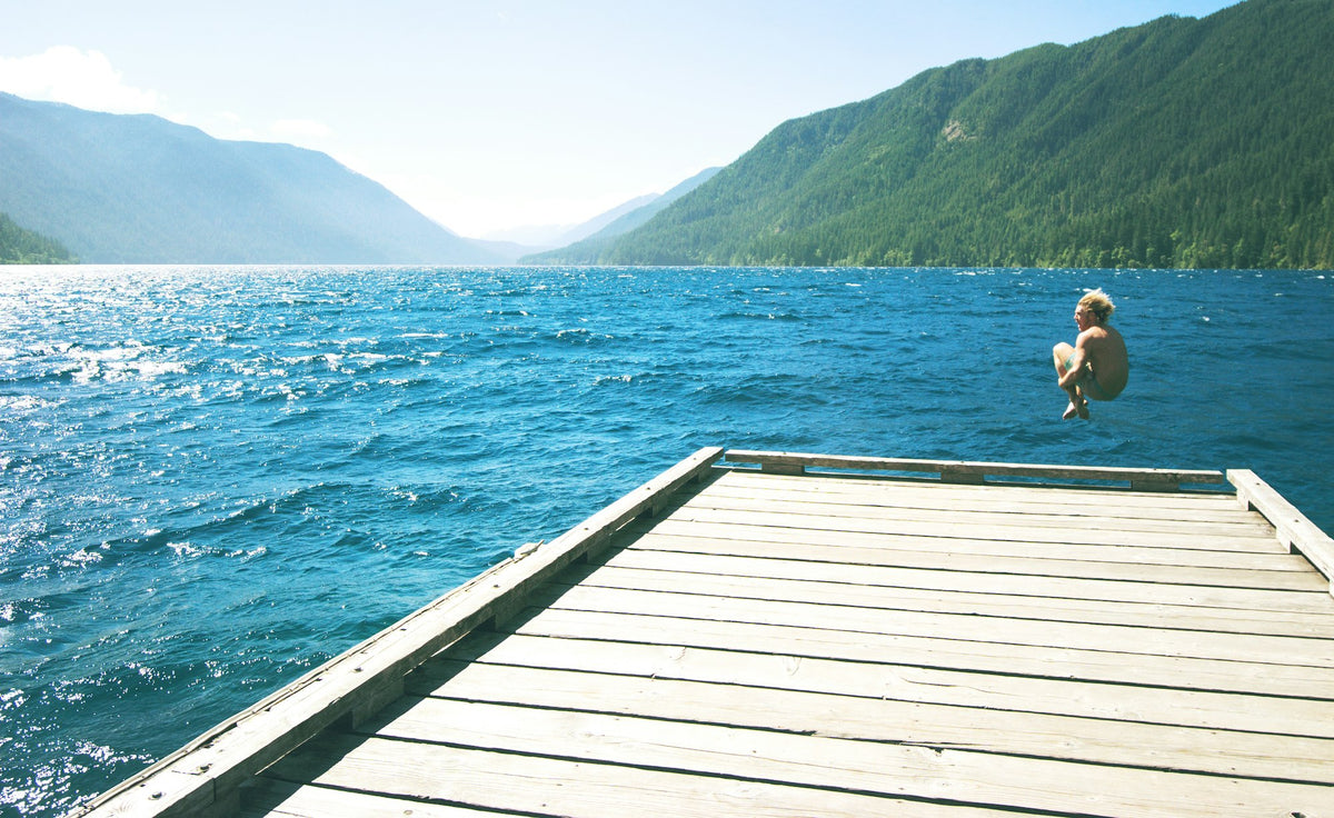 Person leaping off a wooden dock into a lake on a summer day