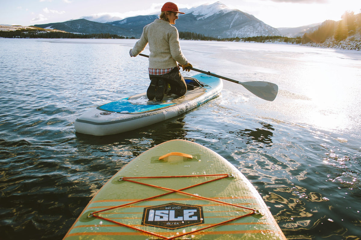 Paddler kneeling on a stand-up paddleboard holding a paddle on calm water