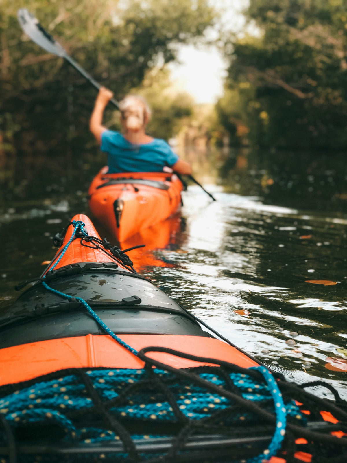 Woman in a kayak mid-stroke holding a double-bladed paddle above the water
