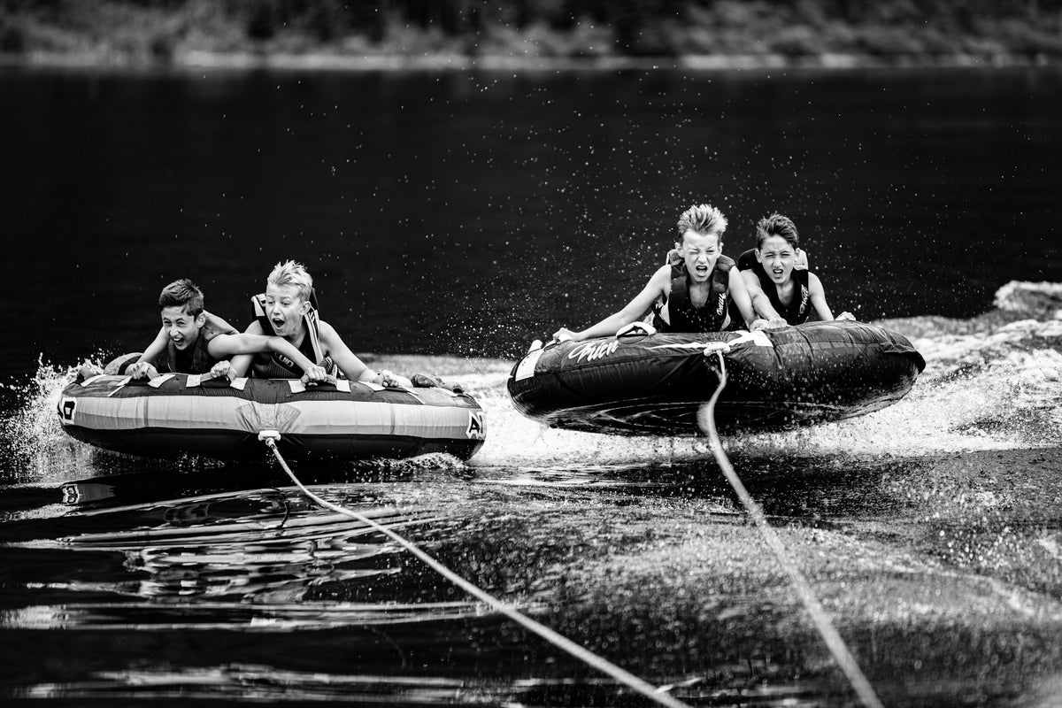 Children riding inflatable towable tubes pulled behind a motorboat