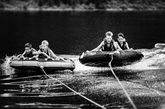 Children riding inflatable towable tubes pulled behind a motorboat