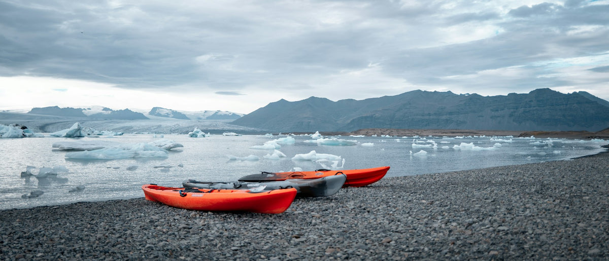Two red kayaks on a rocky shore with icebergs floating in cold water