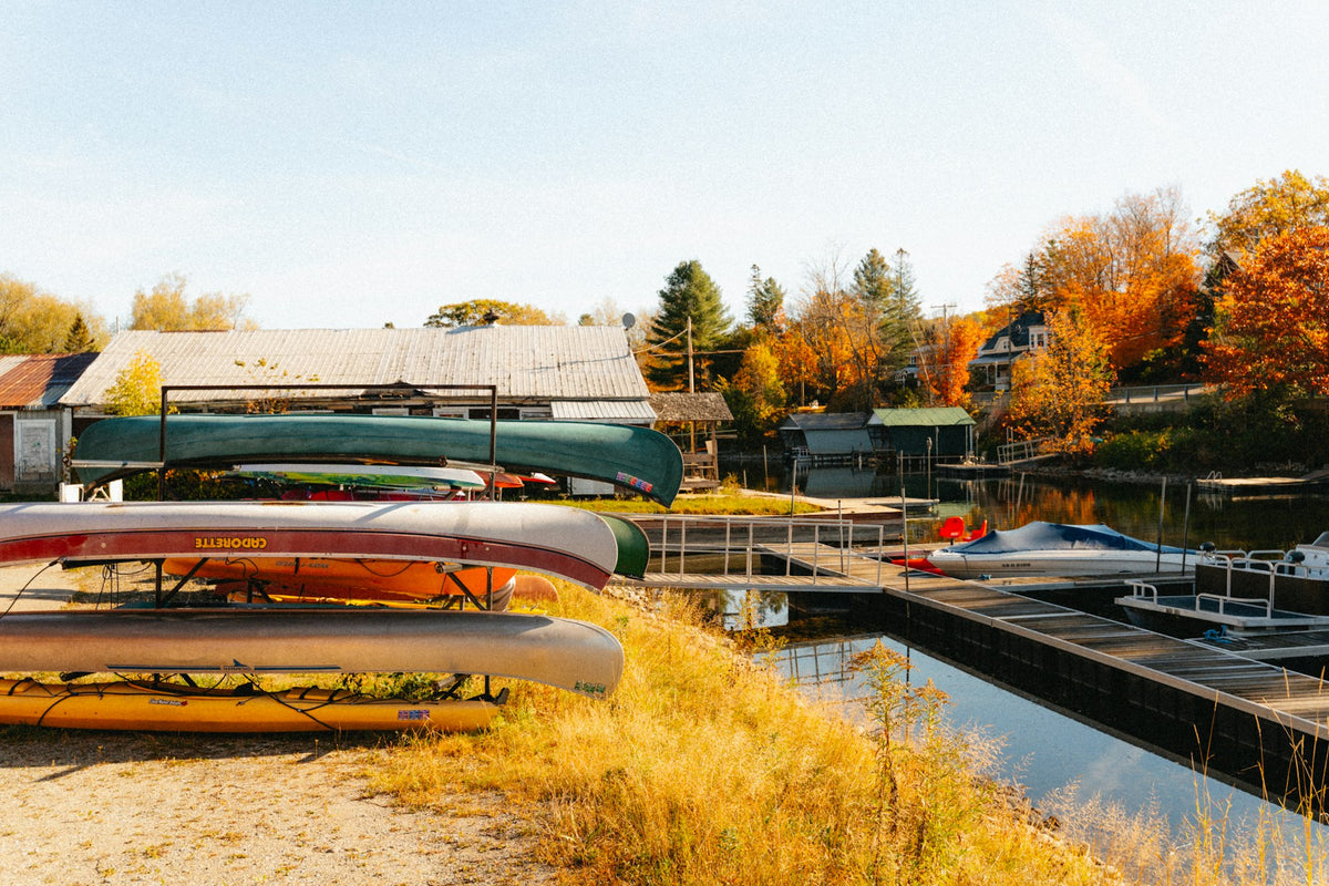 Canoes stacked upside down by a lake with autumn trees behind