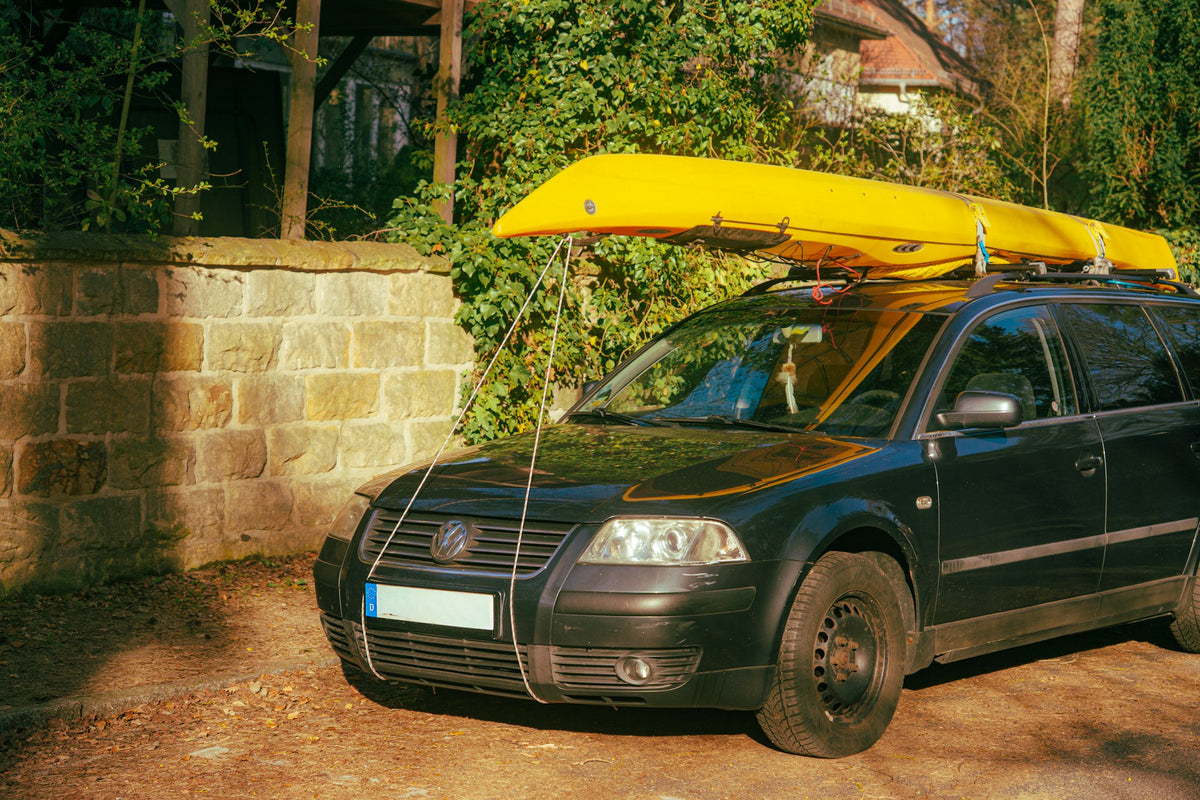 Yellow kayak strapped to the roof rack of a dark station wagon