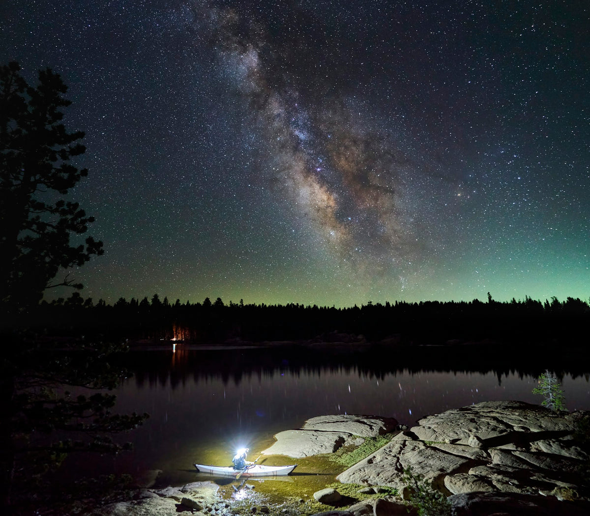 Kayaker wearing a headlamp on a dark lake under the Milky Way